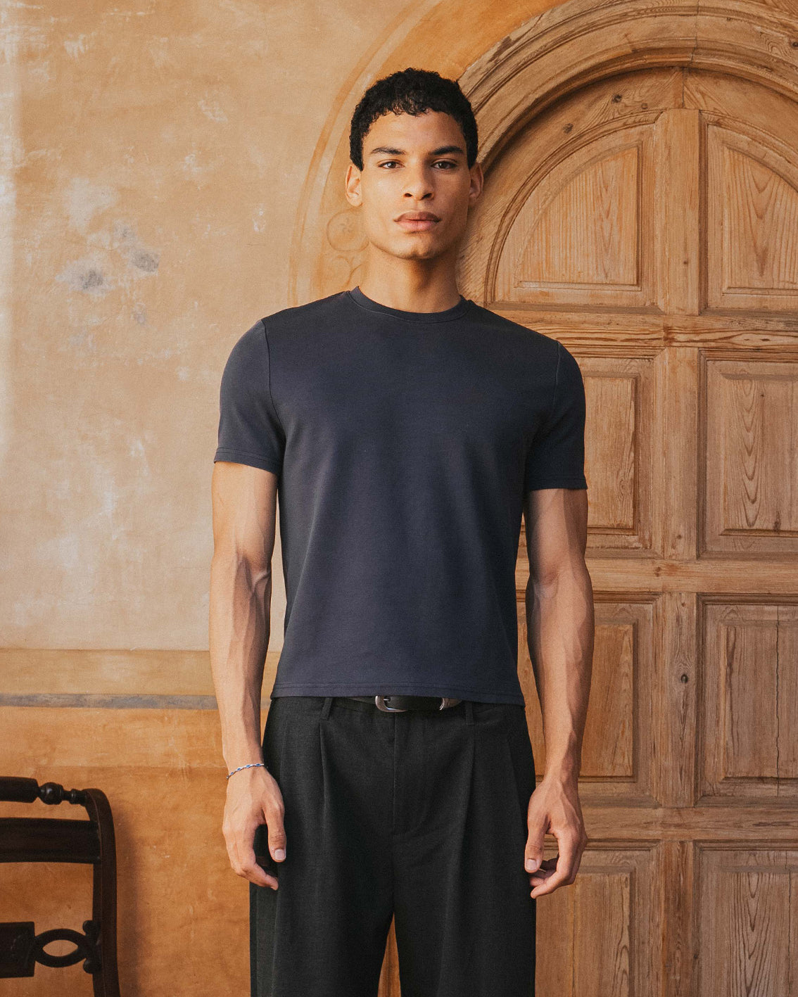 Man wearing a black t-shirt and pants standing in front of a wooden door.